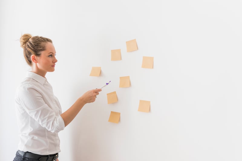 side-view-of-young-business-woman-pointing-toward-stick-notes-on-wall